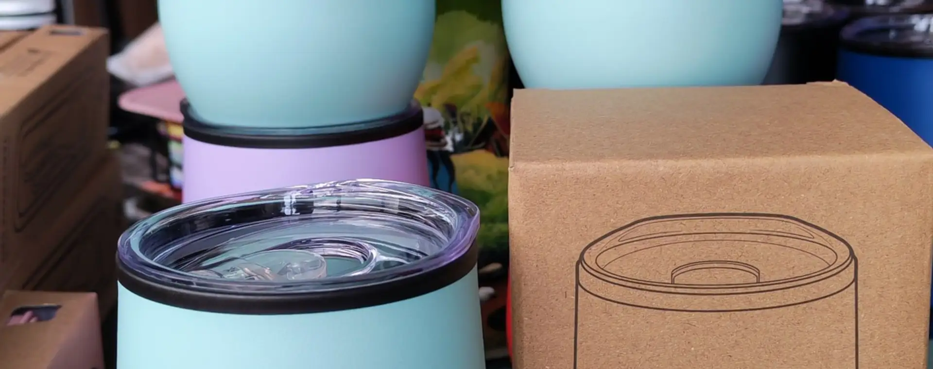 Vasos térmicos de colores apilados junto a una caja kraft