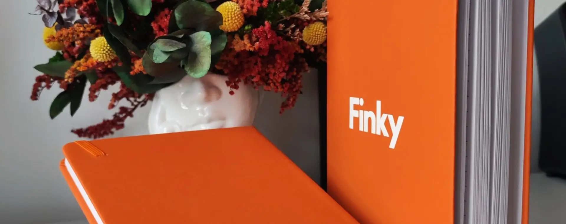 Libreta naranja de tapa dura con logo junto a un arreglo floral