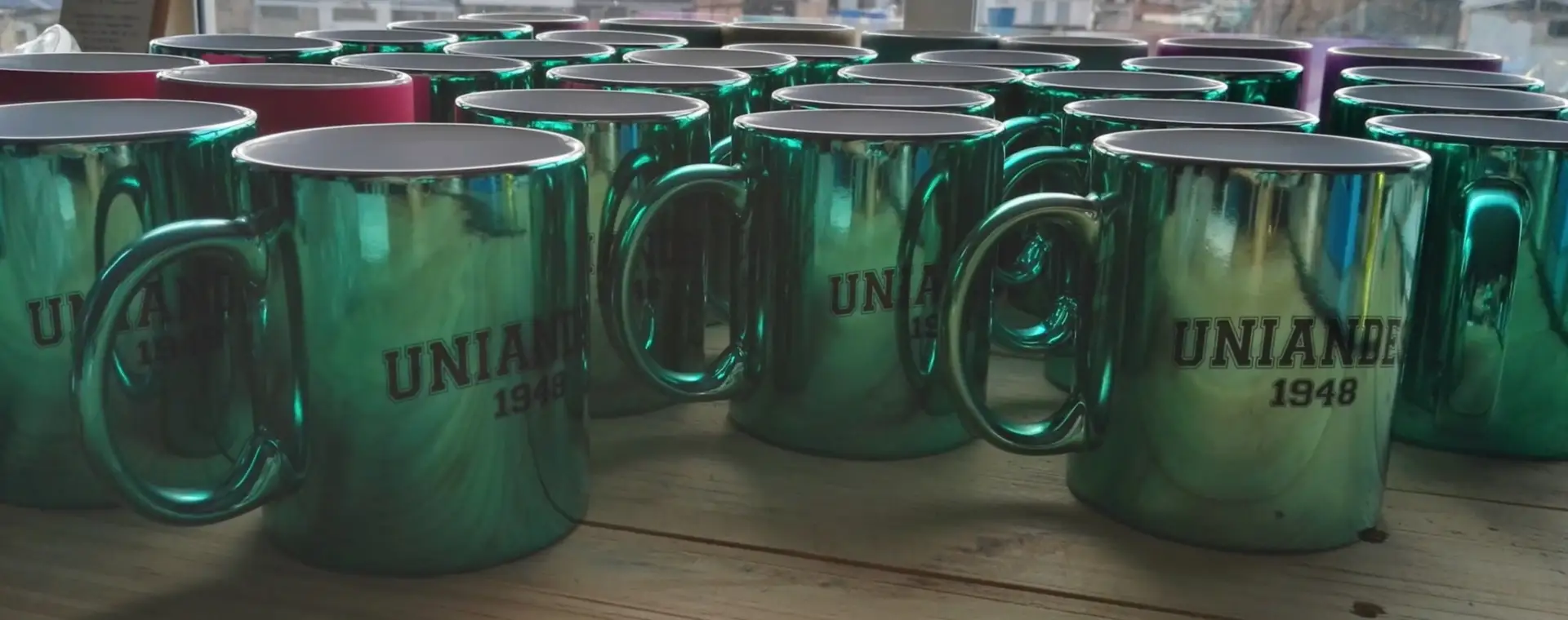 Mugs metalizados verdes personalizados frente a una ventana con vista a la ciudad