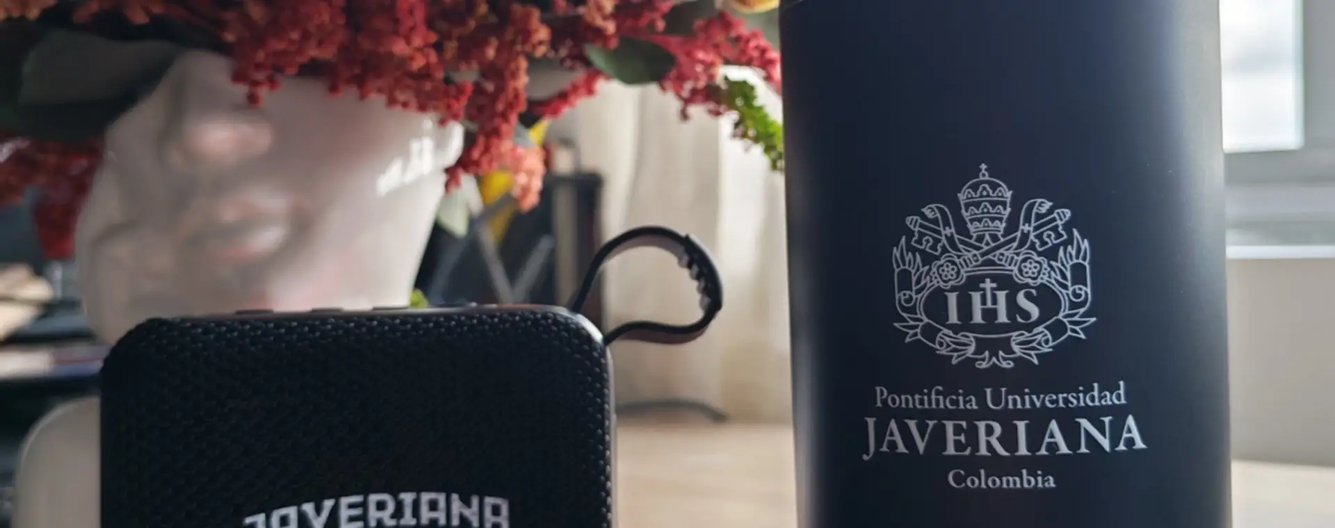Termo negro con escudo grabado con láser junto a un parlante bluetooth personalizado